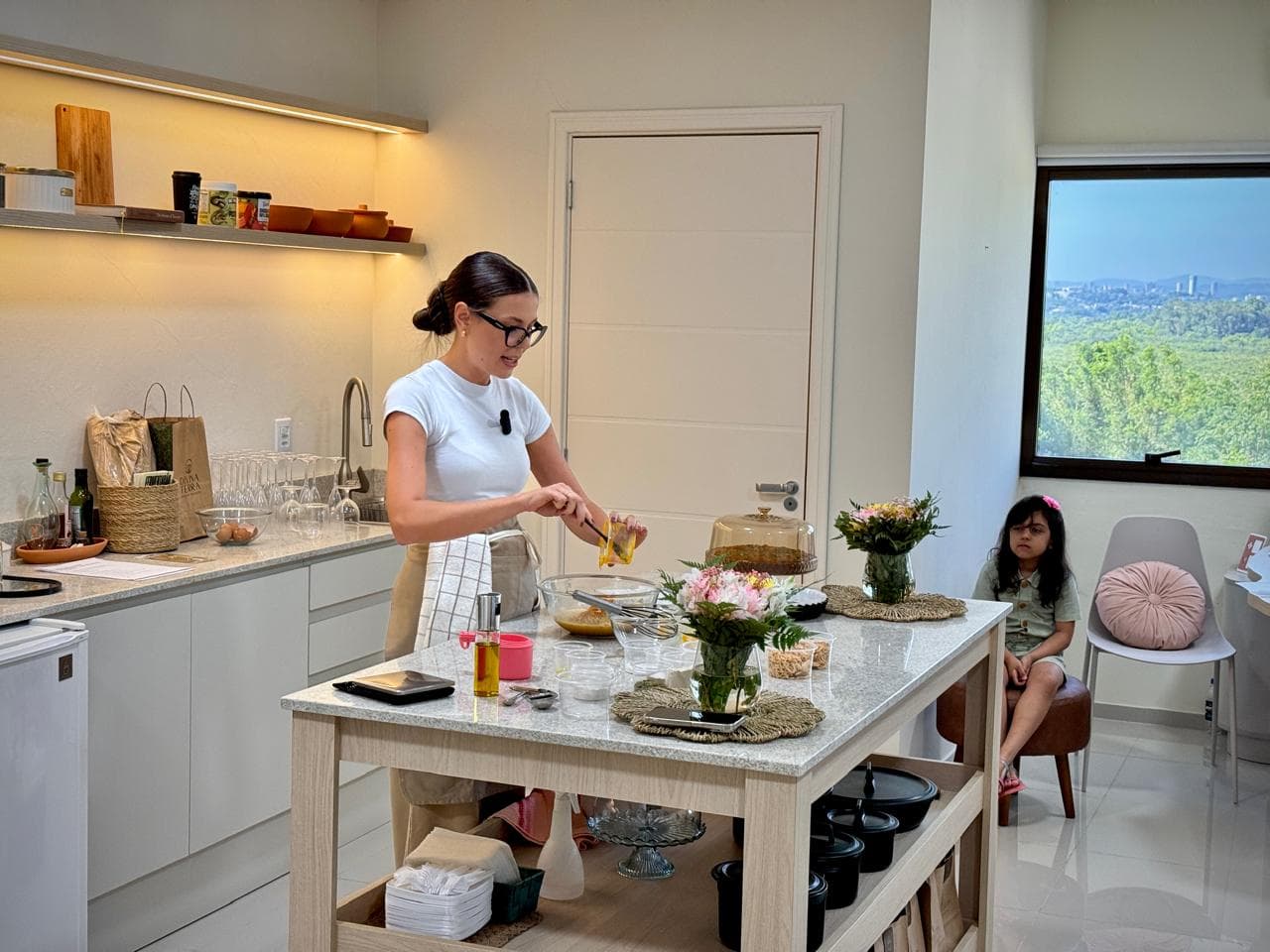 Vanessa na cozinha durante o workshop, com aluna ao fundo.